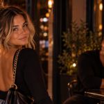 Confident woman walking away from a man who watches her from across a candlelit lounge, representing how pulling back can reveal someone’s interest when you stop chasing their attention.