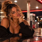 Woman leaning playfully against a car at a gas station at night with a skeptical, unimpressed expression, capturing the humor and disbelief behind recognizing someone else’s bold delusion.