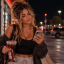 Woman leaving a convenience store late at night, checking her phone with an amused, knowing smirk after receiving an unexpected midnight text.