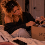 Woman packing away photos and memories from a past relationship, symbolizing the decision to stop holding on, protect her peace, and finally let it end.