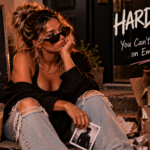 Woman sitting beside battered boxes labeled with empty promises like “maybe,” “what if,” “potential,” and “someday,” representing the hard truth that words without consistent action cannot build a secure future.